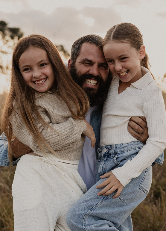 A father laughing while carrying his two daughters outdoors